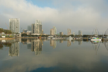 Wide shot Looking north from Demens Landing Park over smooth water with reflections towards city scape of St. Petersburg, Florida . Sailbots in marina with Cloudy blue and white sky with light fog.