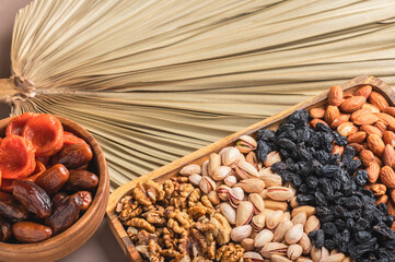 Wooden bowls with date fruits, dried apricots and various nuts on a beige natural background with palm leaves. Islamic religion and Ramadan concept. Traditional, tasty and healthy Ramadan.