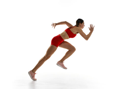 Dynamic side view image of competitive woman in red sportswear, runner in motion, training, running against white studio background. Concept of sport, active and healthy lifestyle, competition