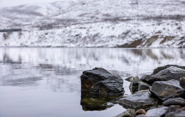 huge sharp stones in water and snow on the river bank with a view of the mountains
