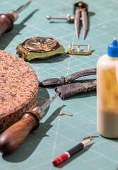 disassembled clock on a table with leather processing tools
