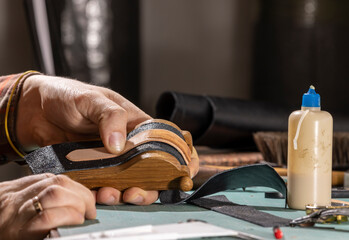 A leather craftsman is making a watch strap.
