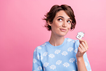 Portrait of charming minded girl hold little paper house look empty space contemplate isolated on pink color background