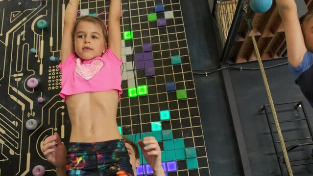 Instructor helps girl to jump off bar supporting with hands. Professional man ensures safe and controlled descent of small child