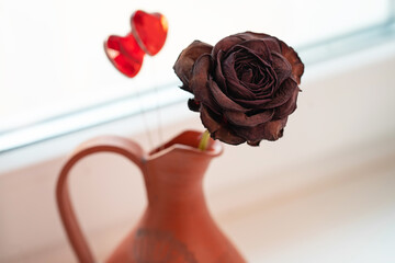 a dried rose in a ceramic jug and two glass hearts in close-up