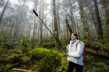 Woman use camera to take photo walk in foggy mist forest in Taipingshan Jianqing Huaigu Trail