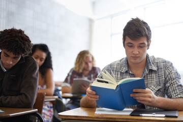 Fototapeta premium University, book and man in classroom reading for development in learning, opportunity and future career. Education, knowledge and growth for college student in lecture, studying for exam or test.