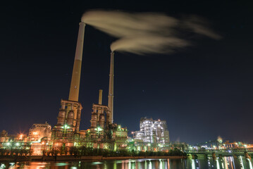 闇夜に浮かぶ光り輝く工場と煙たなびく２本の煙突