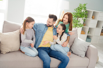 Portrait of four people positive guy embrace adorable girls sit on sofa speak communicating home...