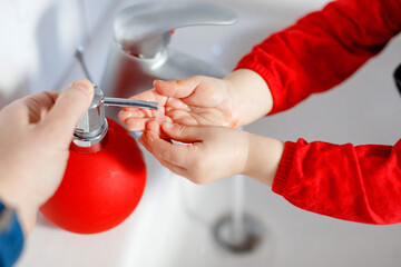 Closeup of little toddler girl washing hands with soap and water in bathroom. Mother or father...