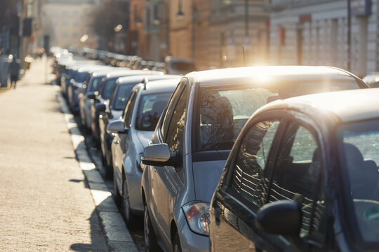 Scenic sunlit view row parked cars on busy city street in european city. Sidewalk parallel side parking full of vehicles traffic jam in downtown on warm sunset evening or sunrise morning
