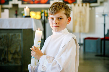 Little kid boy receiving his first holy communion. Happy child holding Christening candle....