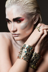 Close portrait of a beautiful blonde girl with bodypainting on her face wearing precious bracelets and rings