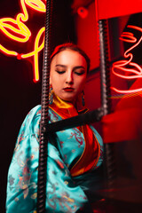 Obraz premium Beautiful girl in kimono. The image of a geisha, Chinese national costume. Background neon. Party concept, night club