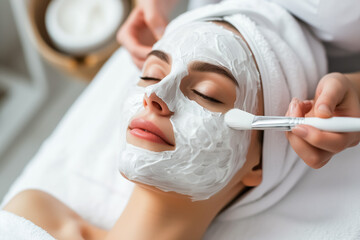 A woman is receiving a facial mask application in a serene spa environment, surrounded by glowing candles, promoting skin health and wellness.