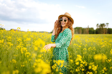 Naklejka na ściany i meble Beautiful woman walking in the blooming field at sunny summer day. Nature, vacation, relax and lifestyle. Summer landscape.