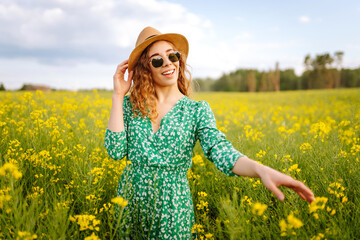 Fototapeta premium Beautiful woman walking in the blooming field at sunny summer day. Nature, vacation, relax and lifestyle. Summer landscape.