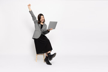 Happy young Asian businesswoman using laptop computer and sitting on wood chair isolated on white...