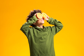 Child boy holding half of orange fruits in front of eyes over yellow background. Healthy food...
