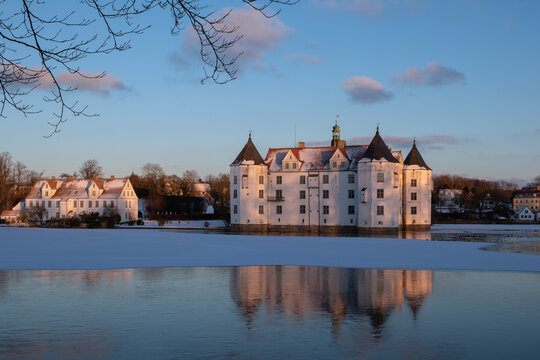 Fairytale water castle in dreamlike winter wonderland with frozen palace pond at sunset..