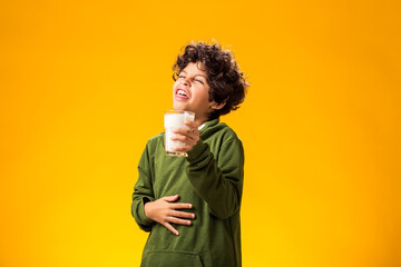 Lactose intolerance. Dairy intolerant child boy with glass of milk feeling over yellow background.