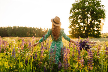 Beautiful woman stands  on blooming fragrant lavender fields. Nature, vacation, relax and lifestyle. Collection of medicinal herbs - obrazy, fototapety, plakaty