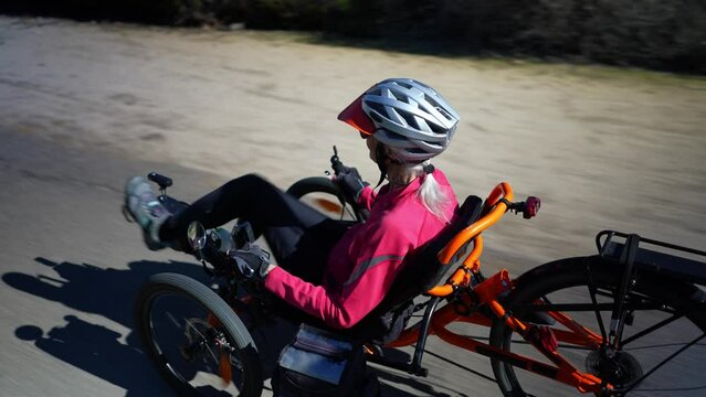 Low angle closeup of elderly senior woman riding recumbent tricycle e-bike on a path on a sunny day in a park.