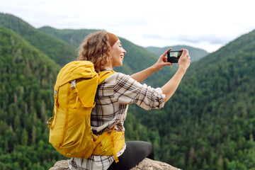 Tourist woman taking picture outdoors for memories, making selfie on top of cliff with valley...