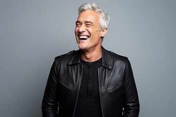 Portrait of a happy senior man in leather jacket posing against grey background.
