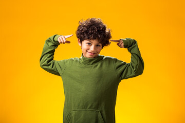 Smiling child boy pointing at camera on yellow background.