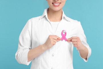 Mammologist with pink ribbon on light blue background, closeup. Breast cancer awareness