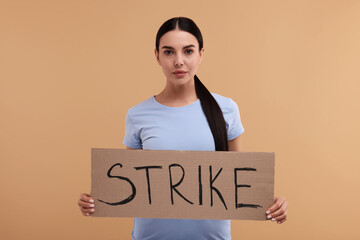 Woman holding cardboard banner with word Strike on beige background