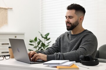 E-learning. Young man using laptop during online lesson at white table indoors