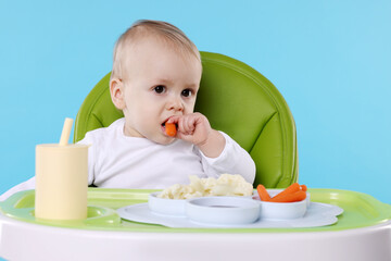 Cute little baby eating healthy food in high chair on light blue background