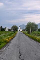 A rural lane, bordered by spring blossoms, draws one towards the Bjornskinn Church on Andoya Island in Northern Norway (Vertical photo)