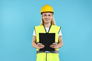 Engineer in hard hat holding clipboard on light blue background