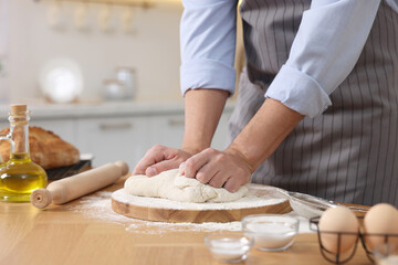 Obraz na płótnie Canvas Making bread. Man kneading dough at wooden table in kitchen, closeup