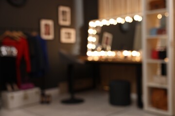 Blurred view of makeup room with stylish mirror on dressing table, chair and clothes rack