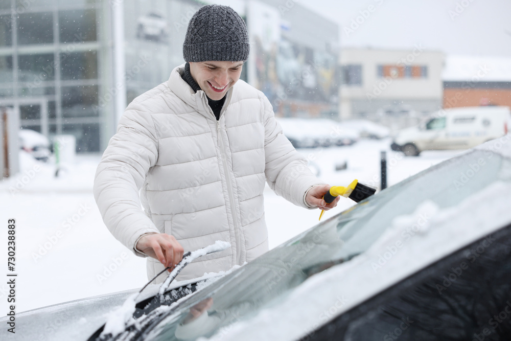 Wall mural man cleaning snow from car windshield outdoors