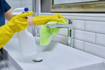 Close-up of cleaning sink with faucet in bathroom, hands in gloves with detergent