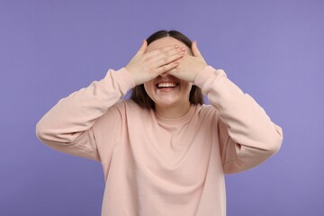 Woman covering eyes and laughing on violet background