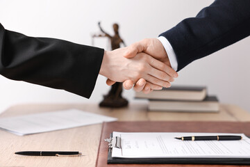 Notary shaking hands with client at wooden table in office, closeup