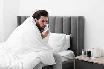 Sick man with tissue coughing on bed at home. Cold symptoms
