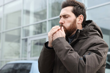 Sick man coughing on city street, space for text. Cold symptoms