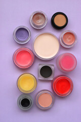 Bowls with various colorful cream beauty products on purple background. Top view.