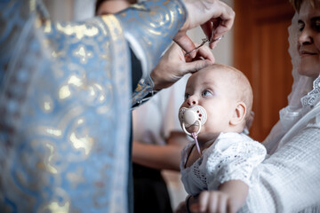 cutting or clipping hair with scissors by a small child in an Orthodox Christian church or temple during the sacrament of baptism with a priest or clergyman - obrazy, fototapety, plakaty