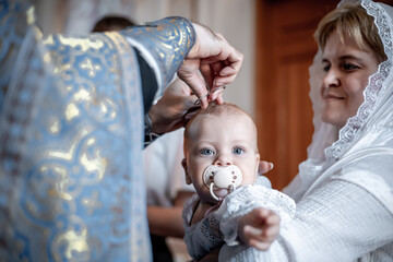 cutting or clipping hair with scissors by a small child in an Orthodox Christian church or temple during the sacrament of baptism with a priest or clergyman - obrazy, fototapety, plakaty