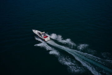 A large red-white boat moves quickly on blue water, moving diagonally, top view. A large boat with...