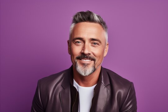 Handsome mature man in leather jacket. Portrait of a handsome mature man looking at camera and smiling while standing against purple background