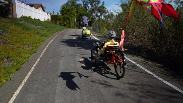 Rear view of mature woman riding a recumbent electric bike with another bike in front pulling a trailer with a dog on a bike path in Southern California. Filmed in slow motion.